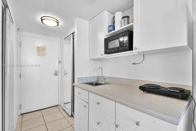 kitchen featuring sink, black microwave, a textured ceiling, white cabinets, and light tile patterned flooring