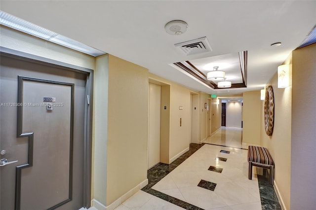 corridor featuring light tile patterned flooring, elevator, and a tray ceiling