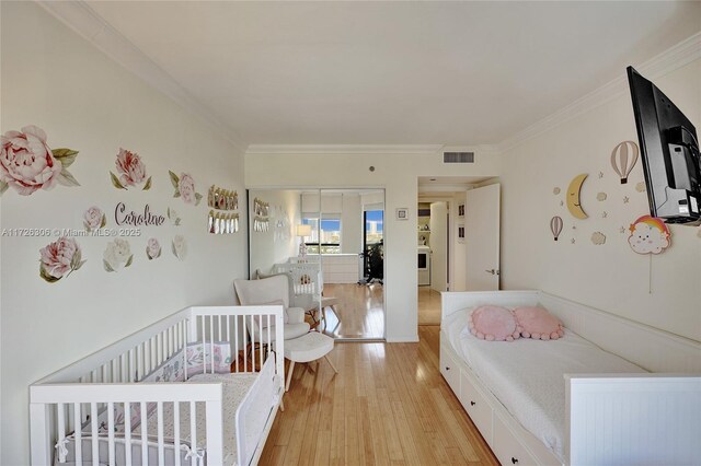 bedroom featuring a crib, ornamental molding, and light hardwood / wood-style flooring