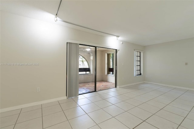 spare room featuring light tile patterned floors, baseboards, and rail lighting