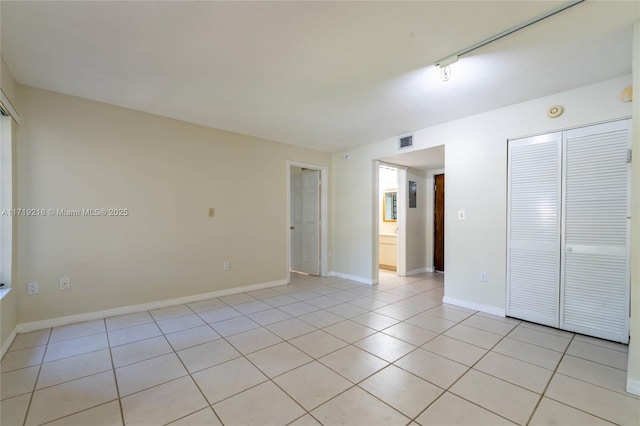 empty room with light tile patterned floors, visible vents, and baseboards