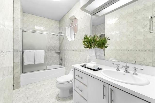 full bathroom featuring tile patterned floors, toilet, bath / shower combo with glass door, tile walls, and vanity