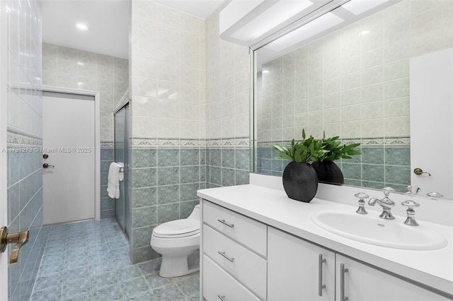 bathroom with vanity, toilet, a shower with shower door, and tile walls