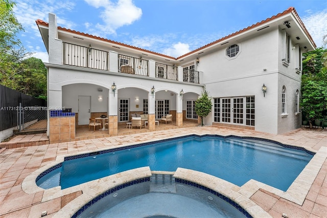 rear view of property with an in ground hot tub, a balcony, a patio area, and french doors