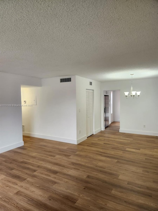 empty room featuring a chandelier, a textured ceiling, and dark hardwood / wood-style flooring