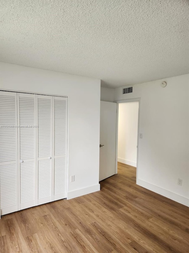 unfurnished bedroom featuring hardwood / wood-style flooring, a closet, and a textured ceiling