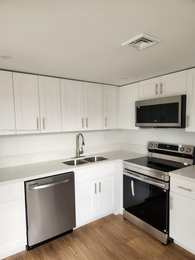 kitchen featuring stainless steel appliances, light hardwood / wood-style floors, sink, and white cabinets