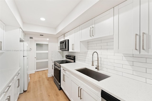 kitchen featuring appliances with stainless steel finishes, sink, white cabinets, light stone counters, and light hardwood / wood-style floors