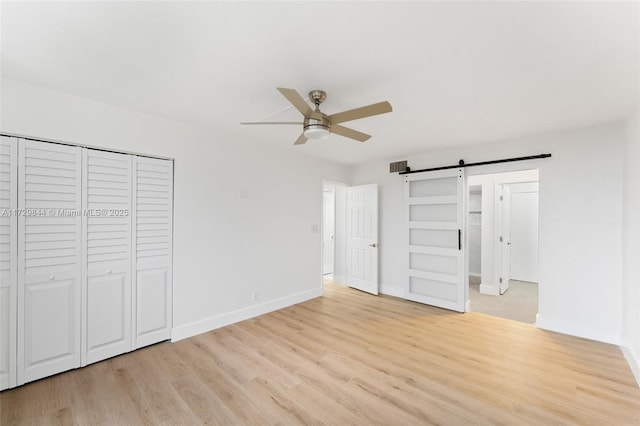 unfurnished bedroom featuring a barn door, light wood-type flooring, ceiling fan, and a closet