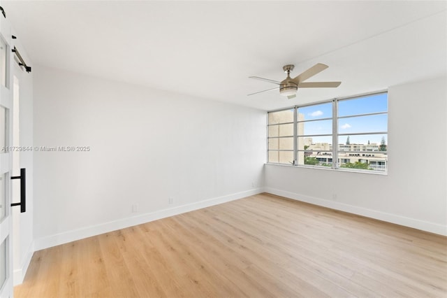 unfurnished room featuring ceiling fan, a barn door, and light wood-type flooring