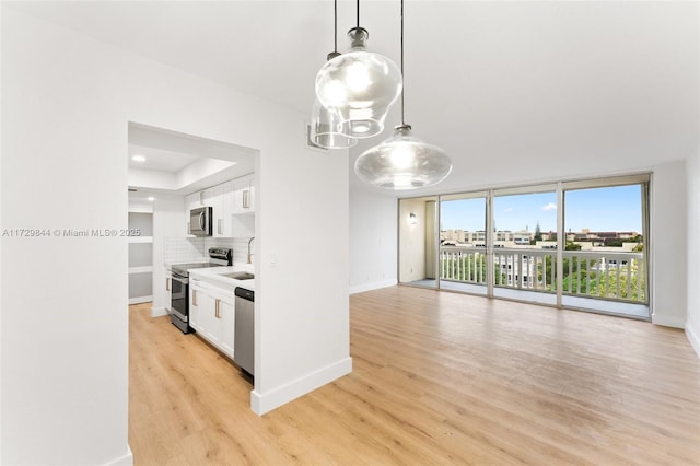 kitchen featuring a wall of windows, appliances with stainless steel finishes, hanging light fixtures, light hardwood / wood-style floors, and white cabinets