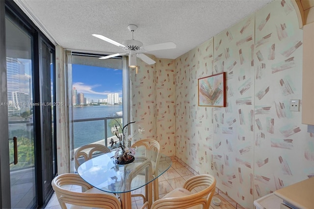 tiled dining space featuring ceiling fan, floor to ceiling windows, a textured ceiling, and a water view