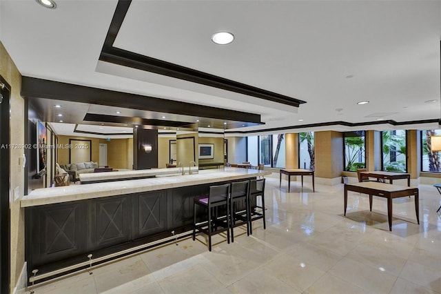 bar with crown molding, light stone counters, and a tray ceiling