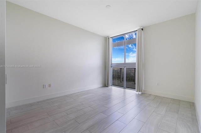 empty room with floor to ceiling windows, baseboards, and wood finished floors