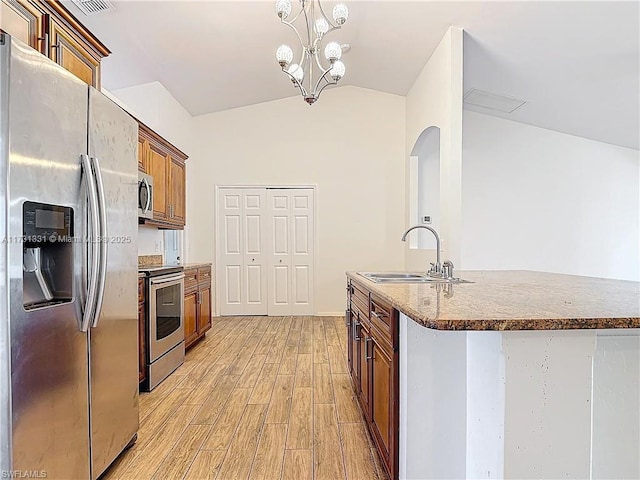 kitchen with appliances with stainless steel finishes, pendant lighting, lofted ceiling, sink, and light hardwood / wood-style flooring