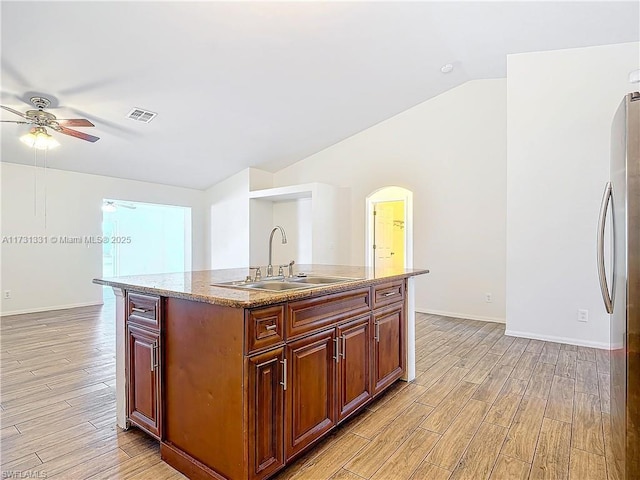 kitchen with sink, vaulted ceiling, light wood-type flooring, stainless steel refrigerator, and a kitchen island with sink