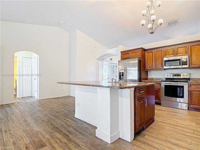 kitchen with stainless steel appliances, vaulted ceiling, a kitchen island with sink, and light wood-type flooring