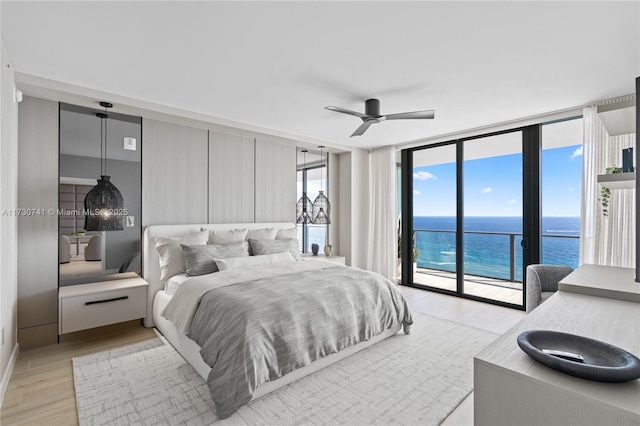 bedroom with ceiling fan, a water view, access to exterior, expansive windows, and light wood finished floors