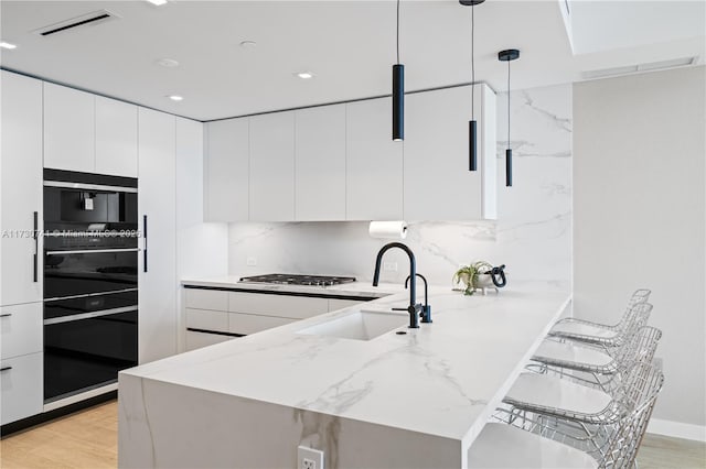 kitchen featuring stainless steel gas cooktop, a peninsula, light wood-style flooring, and white cabinets