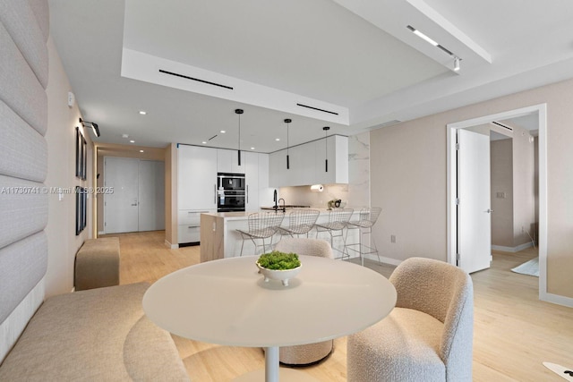 dining area with a tray ceiling, sink, and light hardwood / wood-style flooring