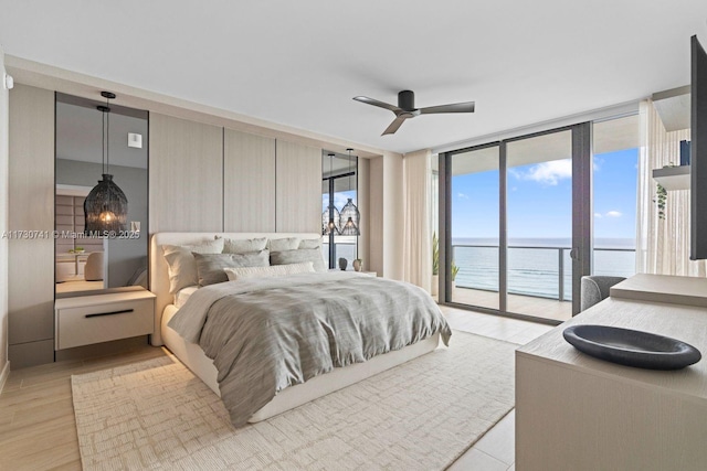 bedroom featuring ceiling fan, floor to ceiling windows, a water view, light hardwood / wood-style floors, and access to outside