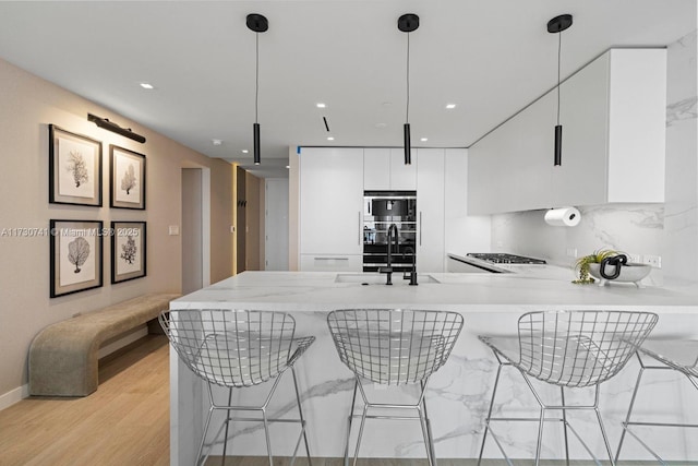 kitchen featuring sink, a breakfast bar, white cabinetry, hanging light fixtures, and kitchen peninsula