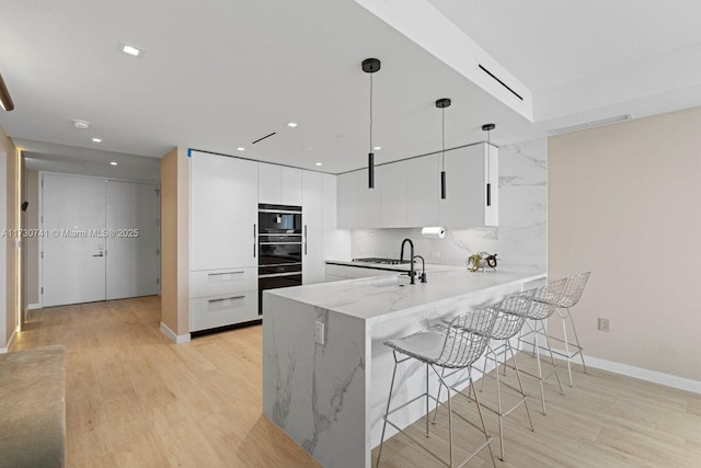 kitchen featuring a breakfast bar area, hanging light fixtures, wall oven, white cabinets, and kitchen peninsula