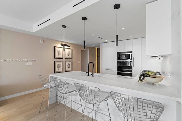 kitchen with a breakfast bar, decorative light fixtures, white cabinets, kitchen peninsula, and light wood-type flooring