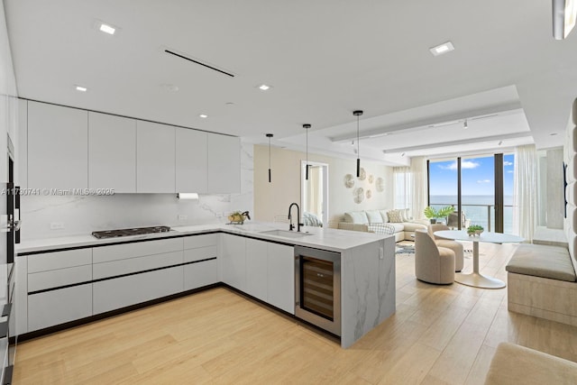 kitchen with white cabinets, beverage cooler, decorative backsplash, hanging light fixtures, and kitchen peninsula