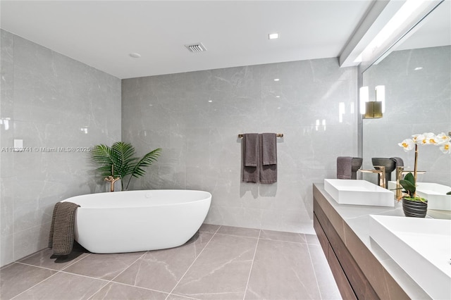 bathroom with tile walls, double vanity, a soaking tub, visible vents, and a sink