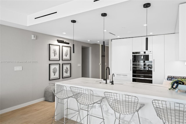 kitchen featuring light wood finished floors, white cabinets, modern cabinets, a peninsula, and light stone countertops