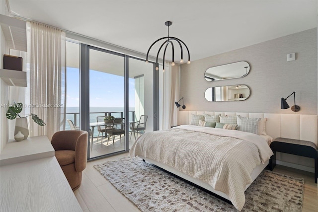 bedroom featuring light wood-type flooring, access to outside, a wall of windows, and a water view