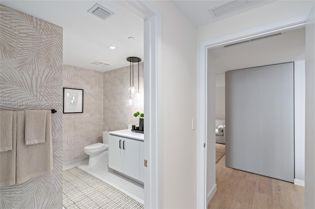 half bathroom featuring visible vents, toilet, vanity, wood finished floors, and wallpapered walls