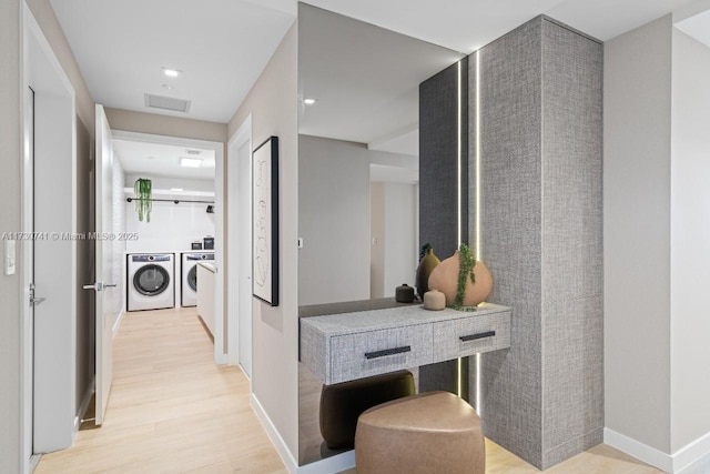 corridor with light wood-style flooring, visible vents, baseboards, and washing machine and clothes dryer