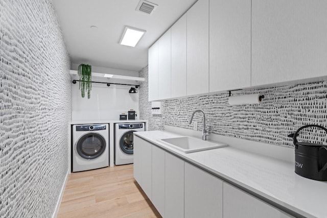 clothes washing area with washer and clothes dryer, light wood finished floors, cabinet space, visible vents, and a sink