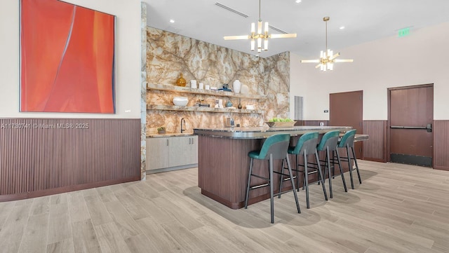 bar with a wainscoted wall, light wood finished floors, visible vents, a towering ceiling, and a chandelier