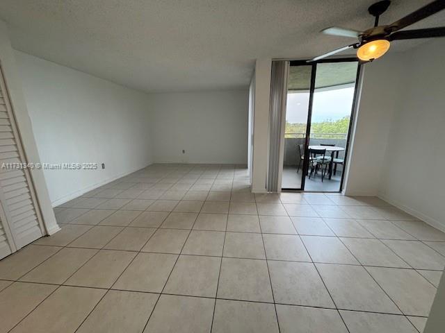 empty room with floor to ceiling windows, light tile patterned flooring, a textured ceiling, and ceiling fan