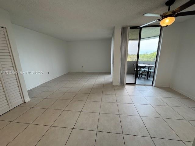 tiled empty room with floor to ceiling windows, ceiling fan, and a textured ceiling