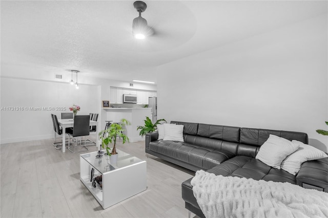 living room featuring a textured ceiling, light wood-style floors, visible vents, and baseboards