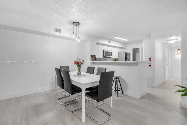 dining area with light wood-type flooring, baseboards, visible vents, and a textured ceiling