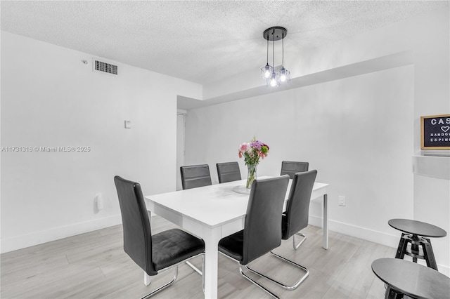 dining space featuring light wood-style floors, visible vents, a textured ceiling, and baseboards