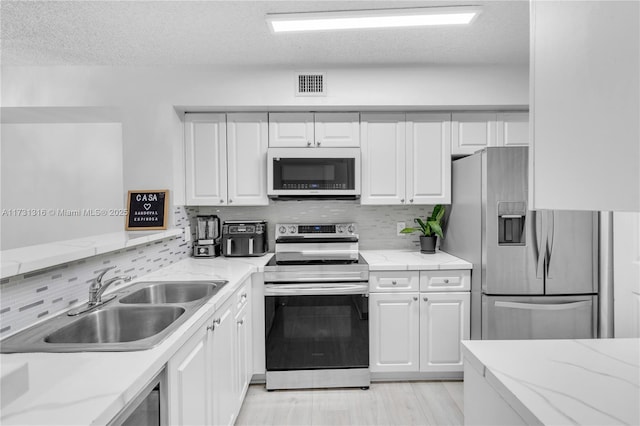 kitchen featuring stainless steel appliances, a sink, visible vents, white cabinets, and decorative backsplash