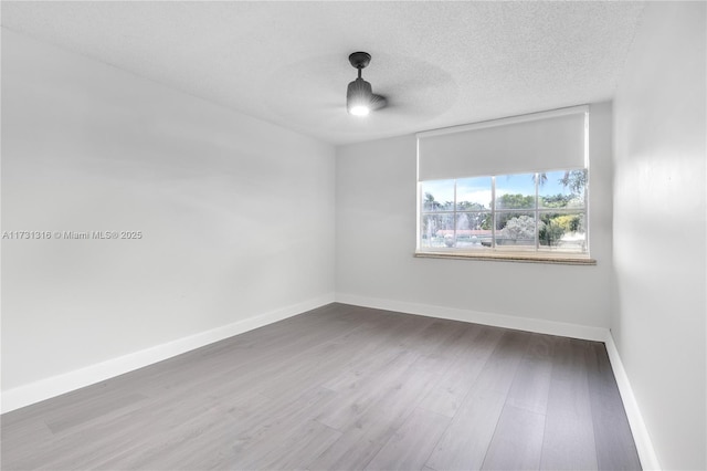 unfurnished room featuring a textured ceiling, wood finished floors, and baseboards