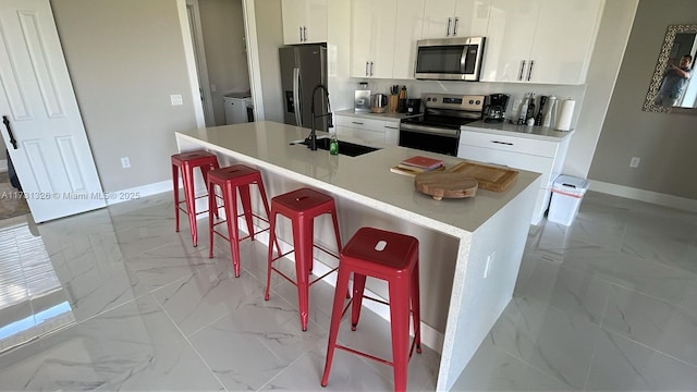 kitchen featuring appliances with stainless steel finishes, a kitchen breakfast bar, a center island with sink, and white cabinets