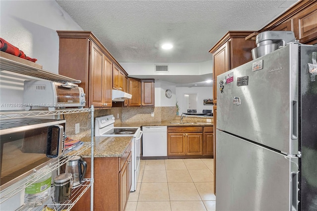 kitchen with light tile patterned flooring, tasteful backsplash, sink, light stone counters, and white appliances