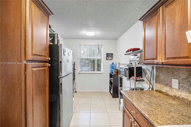 kitchen featuring light tile patterned floors, refrigerator, light stone countertops, a textured ceiling, and decorative backsplash