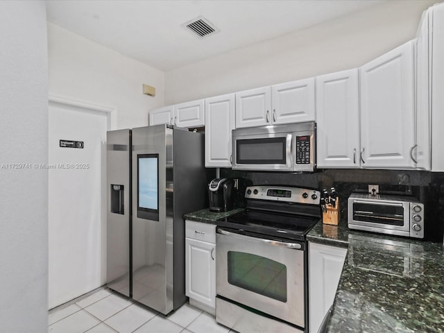 kitchen featuring white cabinetry, light tile patterned floors, dark stone counters, and appliances with stainless steel finishes