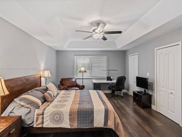 bedroom featuring dark hardwood / wood-style floors, a raised ceiling, ceiling fan, and two closets