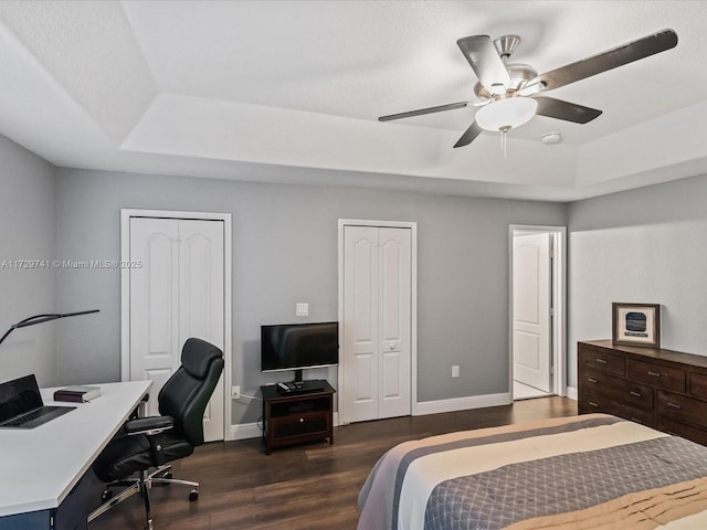 bedroom featuring multiple closets, ceiling fan, a tray ceiling, and dark hardwood / wood-style flooring