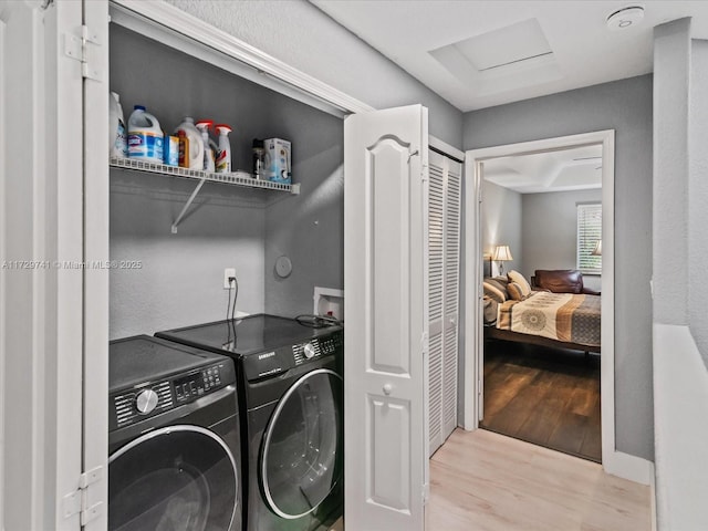 clothes washing area with washer and clothes dryer and light wood-type flooring